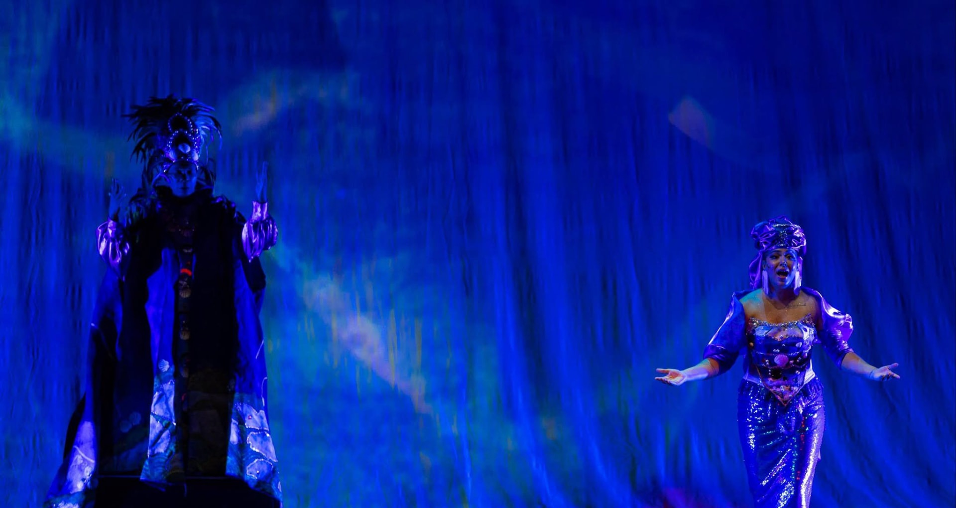 Two performers in luminous costumes on the blue-lit stage of the Ziff Ballet Opera House during Ayiti Bèl Nanm