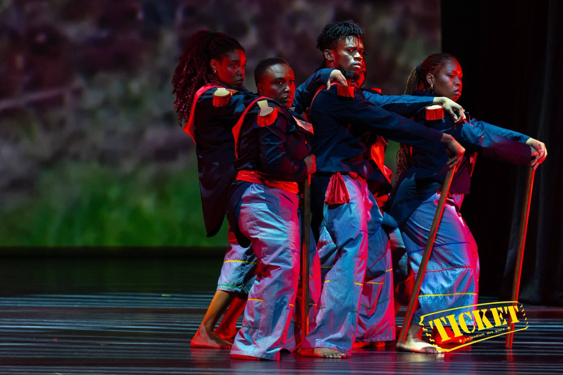 Four dancers with staffs in indigo and red stage light